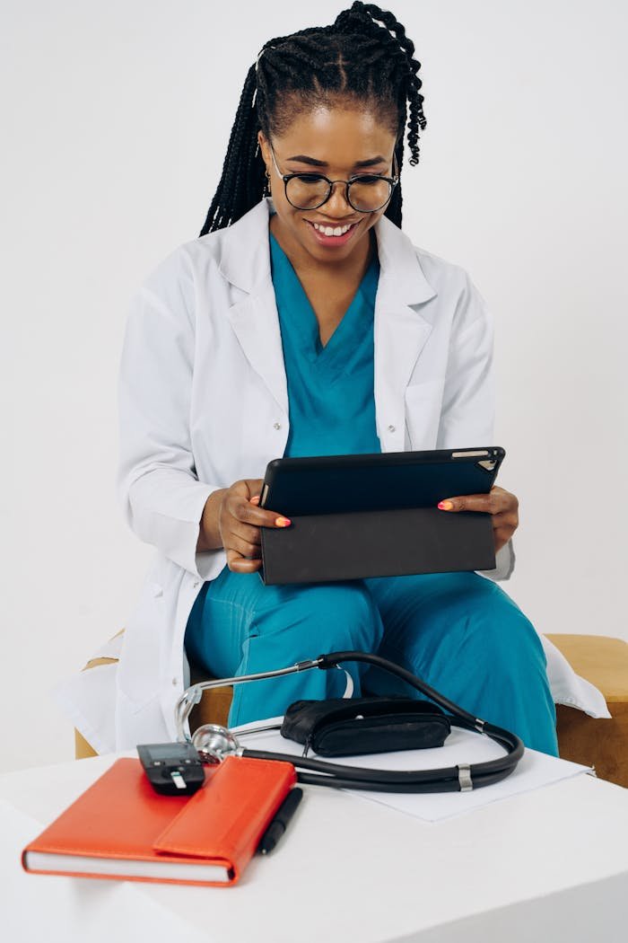 Black female doctor in scrubs using a tablet for virtual consultation indoors.