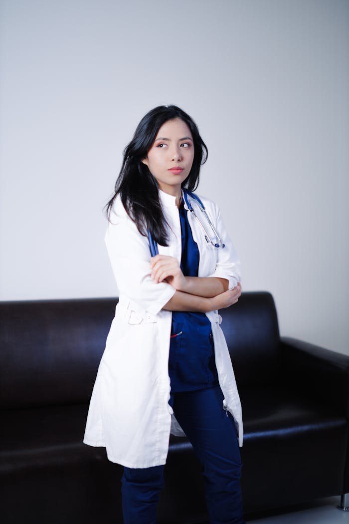 A confident female doctor stands in a clinic setting, wearing a lab coat.