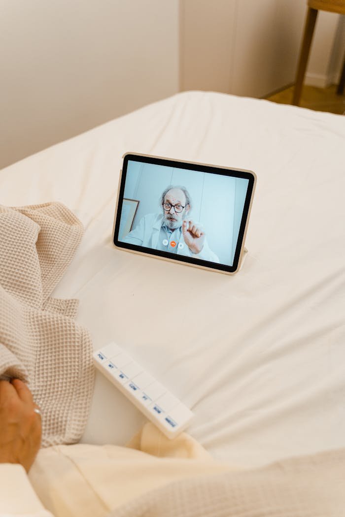 A digital tablet on a bed showing a doctor conducting an online consultation via video call.