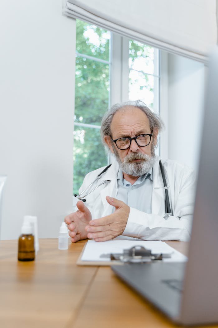 Senior doctor with glasses explaining during an online video call from his desk.